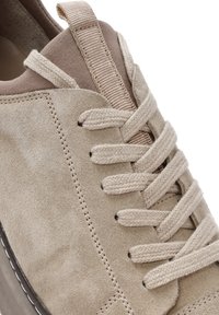 Baskets en cuir suédé beige avec des lacets tressés épais, des coutures détaillées et une languette en tissu rembourrée.