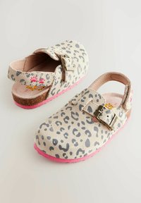 Mules en imprimé léopard avec une tige en daim, taches grises sur un fond beige, semelle en caoutchouc rose et fermeture à boucle en métal.