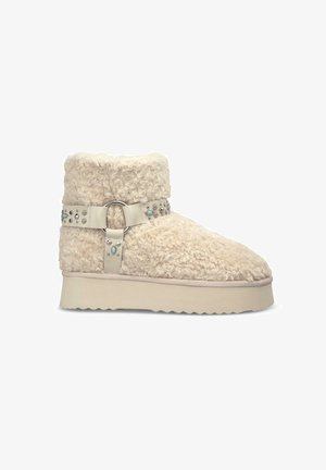 Beige faux fur ankle boots with a flat, textured sole and an adjustable leather strap featuring metal studs and a circular buckle.