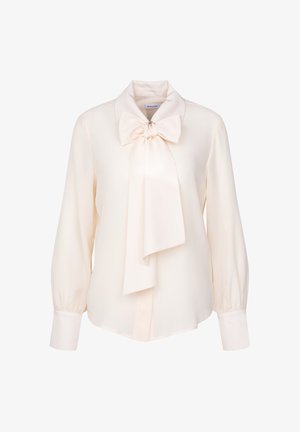 Blouse de couleur crème avec un large col à nœud, des manches longues bouffantes et des poignets boutonnés. Fabriquée dans un tissu lisse et léger.