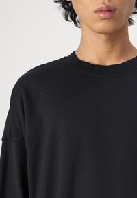 Black long-sleeve t-shirt made of smooth cotton. Features a ribbed neckline and relaxed fit with dropped shoulders and minimal stitching detail.