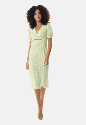 Green and white gingham mid-length dress with puff sleeves, wrap front, and cutout detail. Paired with green open-toe heels.