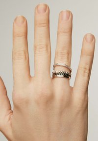 Anillos apilados en tonos de plata y oro, con superficies texturizadas y diferentes anchos. El diseño incluye bandas lisas junto a acentos con tachuelas.