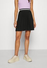 Gonna nera plissettata con una vita a righe orizzontali a contrasto. Abbinata a sneakers platform di colore chiaro.