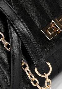 Black leather handbag with a textured finish. Features a gold chain accent and a rectangular clasp. Compact shape, sturdy handles.