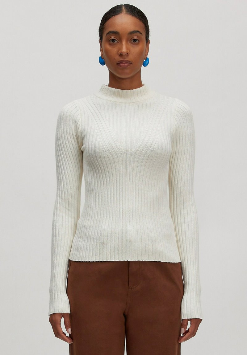 Cremfarbener Rippstrickpullover mit hohem Ausschnitt und langen Ärmeln, der dezente vertikale Streifen und eine figurbetonte Silhouette aufweist.