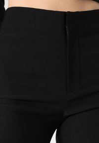 Calças pretas de cintura alta com uma textura suave, apresentando um fecho discreto e linhas limpas para uma aparência elegante.