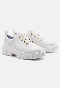 Baskets à plateforme blanches avec une tige en tissu texturé, des œillets dorés et une semelle épaisse et rainurée pour plus de hauteur et de maintien.