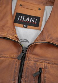 Braune Lederjacke mit Reißverschluss vorne, mit einer strukturierten Oberfläche, zwei Taschen und einem Etikett mit der Aufschrift "JILANI COLLECTION" in Größe 50.