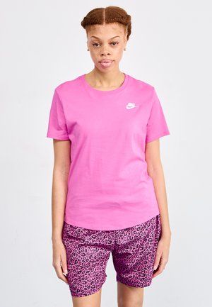 T-shirt in cotone rosa con maniche corte e logo Nike bianco. Abbinato a pantaloni corti rosa con un motivo a macchie di leopardo nere.
