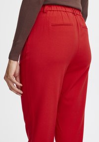 Rode, elastische taillebroek met zijzakken, een gladde textuur en een op maat ontworpen stijl. De achterkant heeft twee verticale decoratieve naden.