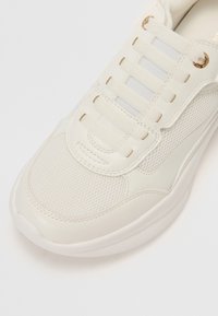 Baskets blanches avec bout en mesh, superpositions en cuir et lacets élastiques sans nœud maintenus par des œillets dorés.