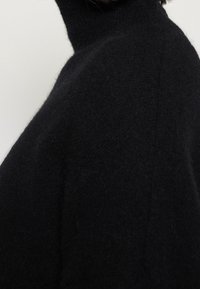 Zwarte coltrui gemaakt van zachte, gestructureerde stof. Heeft een aangesloten pasvorm met een naadloze afwerking en een minimalistische stijl.