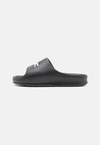 Sandal din cauciuc negru, cu o textură netedă, design cu vârful deschis și talpă ridicată. Prezintă un logo alb pe partea superioară.
