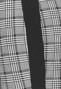 Svart och vit rutig tyg med en slät svart panel, som har en blandning av rutnät och hundtandsmönster, vilket skapar en tydlig visuell kontrast.