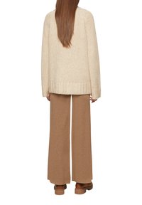 Beige gebreide trui met ribbels aan de onderkant, gecombineerd met lichtbruine wijde broeken. Gestructureerde stof, relaxte pasvorm en lange mouwen.