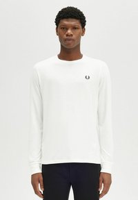 Camisetta bianca a maniche lunghe con scollo tondo, caratterizzata da un piccolo logo nero sul lato sinistro del petto. Tessuto di cotone morbido, design semplice.