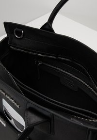 Mustat kassi, jossa on teksturoitu pinta, varustettuna vetoketjullisella pääosastolla, kahdella sisätaskulla ja sileällä kahvalla.