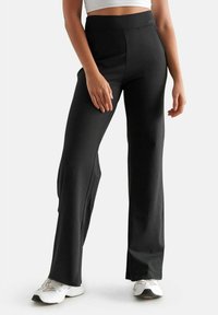 Pantaloni sportivi neri, aderenti, con vita alta, texture liscia e gambe larghe. Indossati con sneaker bianche per creare un contrasto.
