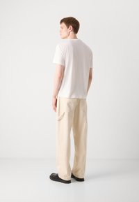 Hvid t-shirt med korte ærmer parret med lyse beige cargo-bukser med sidelommer og sorte sko. Glat tekstur med en afslappet pasform.