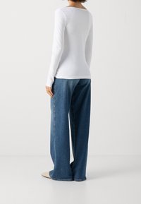 Vit långärmad topp matchad med löst sittande, högmidjade blå jeans. Slät tyg med en subtil lyster och rak benmodell.