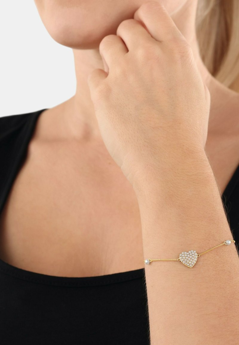 Bracciale d'oro con un pendente a forma di cuore adornato con cristalli trasparenti, collegato da catene sottili e impreziosito da piccoli perline.