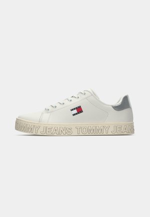 Balta kedu ar gludu ādas augšdaļu, pelēka akcenta ap papēdi un bieza, bēša zole ar "TOMMY JEANS" zīmola uzrakstu.