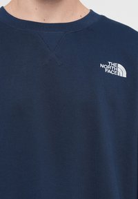 Navy blue sweatshirt made from a soft fabric, featuring a round neck, cross-stitch detail, and white embroidered logo on the chest.