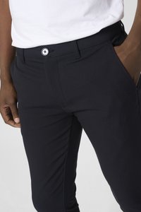 Pantalones negros de tejido suave con un diseño ajustado, bolsillos frontales y un botón a contraste en la cintura con un logo decorativo.