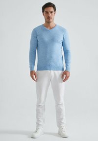 Pull bleu clair en V en matière douce et texturée, associé à un pantalon blanc et des baskets blanches. Design simple, coupe ajustée.