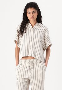 Chemise cropped en mélange de lin beige clair avec des rayures verticales bleu marine, dotée d'un col structuré et de manches courtes décontractées. Associée à un pantalon assorti.