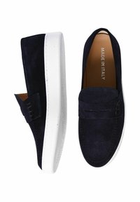 Scarpe slip-on in suede blu navy con suole in gomma bianca. Presentano un piccolo elemento decorativo sul lato e una fodera interna liscia etichettata "Made in Italy."