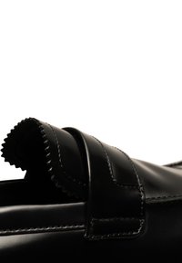 Svart lädersko med en böjd, texturerad klaff som är fäst med ett spänne. Slät yta med synlig sömnad och vågig kantdetalj.