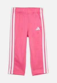 Rožinės sportinės kelnės, pagamintos iš minkštos medžiagos, su baltais šonų dryžiais ir "Adidas" logotipu priekyje. Sukurtos patogumui ir lankstumui.