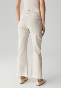 Lichtgekleurde spijkerbroek met een flared model, met achterzakken en een wit label op de tailleband. De stof heeft een soepele textuur en minimale details.