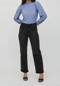 Vaaleansininen pitkähihainen paita, jossa on neulottuja kuvioita ja gathered-hartiat; korkeavyötäröiset mustat farkut; mustat avonaiset korkokengät.