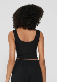 Top corto nero a costine con scollo rotondo e spalline larghe, realizzato in tessuto elasticizzato. Il design presenta una silhouette aderente.