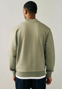 Sudadera de algodón verde oliva con cuello redondo, puños y dobladillo acanalados. Textura suave, corte casual, vista desde la parte de atrás.