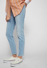 Ljusblå denimjeans med smal passform, med en diskret sliten detalj. Matchas med vita sneakers och en rosa randig skjorta.