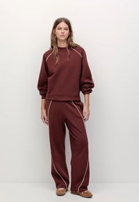 Burgundowy sweatshirt z bufiastymi rękawami i białymi wykończeniami, w połączeniu z dopasowanymi spodniami. Miękki materiał, luźny krój, minimalistyczne detale.
