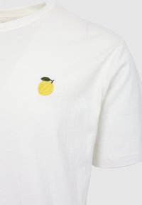 Λευκό πουκάμισο με κοντά μανίκια με μικρή κίτρινη λεμονιά κεντημένη και πράσινο φύλλο στην αριστερή περιοχή του στήθους.