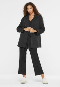 Dark gray, textured suit with oversized blazer and wide-leg trousers. Worn over a matching vest, paired with white sneakers.