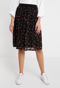 Svart plisserad kjol med blommönster i rött och grönt. Elastisk midja, genomskinligt material, kombinerad med vita sneakers.