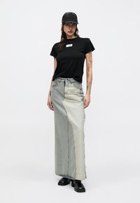 Μαύρο μπλουζάκι με ετικέτα, συνδυασμένο με φούστα από δύο τόνους τζιν με ξεφτισμένα άκρα και μαύρες μποτάκια αστραγάλου. Το μοντέλο φοράει μαύρο καπέλο.