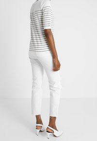 Proužkovaný bílý a šedý krátký rukáv, doplněný bílými roztrhanými džíny a bílými sandály na podpatku. Hladká textura a ležérní střih.