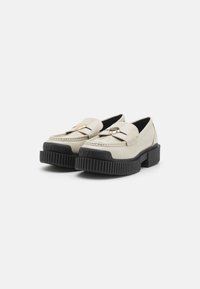 Chunky platform loafer met een soepele crème leren bovenkant. Voorzien van een goudkleurig hardwareaccent en een structuur zwarte rubberen zool.