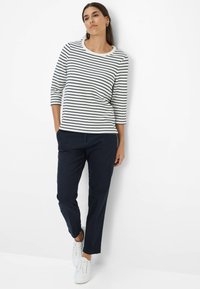 Gestreiftes, weißes und dunkelblaues Langarmshirt, dunkelblaue Hose und weiße Sneakers; lockere Passform mit Rundhalsausschnitt und 3/4-Ärmeln.