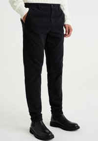 Černé manšestrové kalhoty s texturovaným povrchem, rovného střihu, s bočními kapsami a knoflíkovým zapínáním. V kombinaci s černými kotníkovými botami.