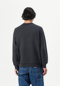 Mørkegrå hettegenser med rund hals, senkede skuldre og ribbestrikkede mansjetter, sammen med blå cargo-jeans, sett fra baksiden.