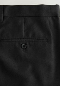 Pantalons en tissu noir avec une poche arrière dotée d'un bouton noir unique et de détails cousus, présentant une texture lisse et un design ajusté.